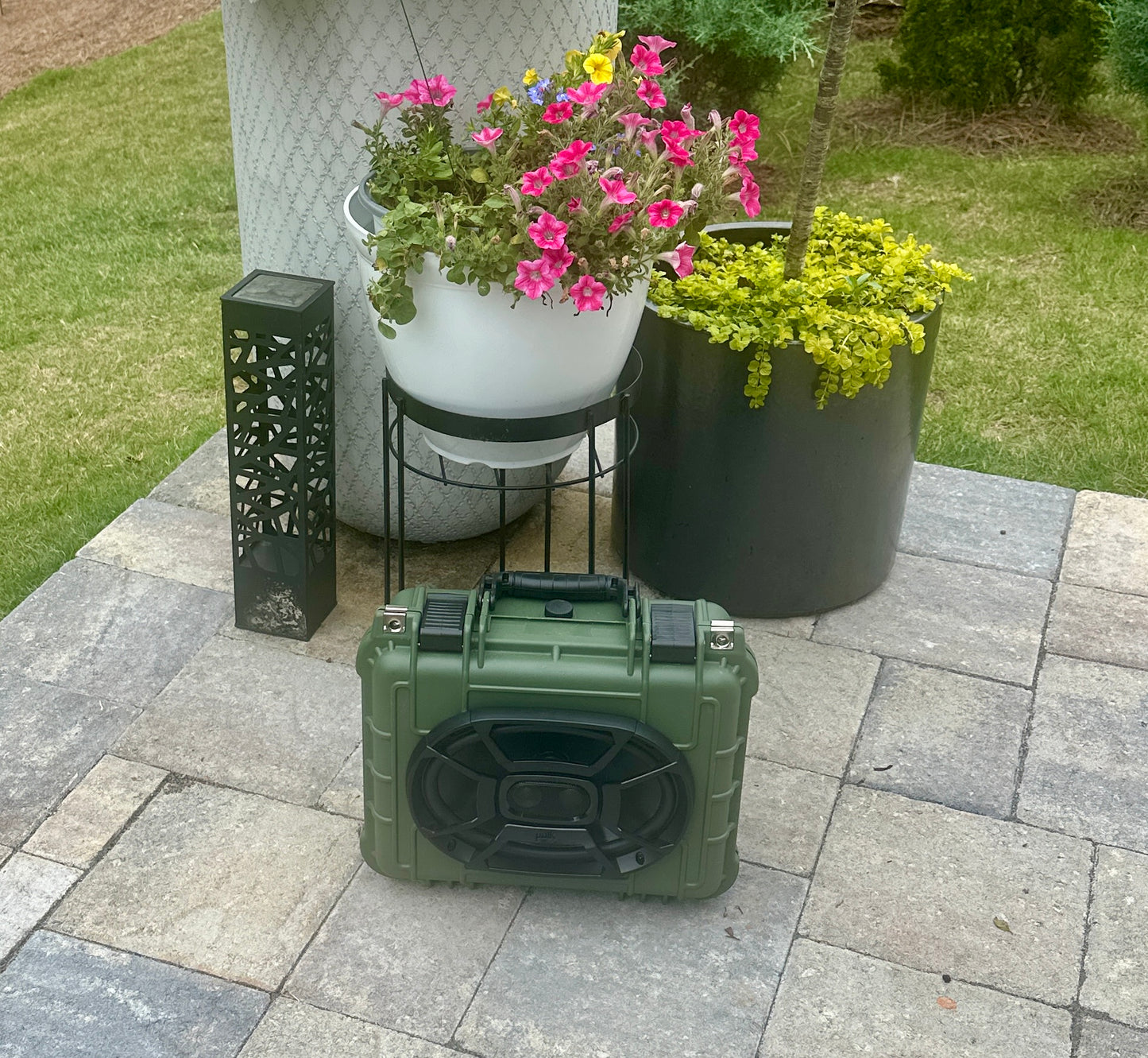 Green portable speaker on a patio with potted plants and a lantern.