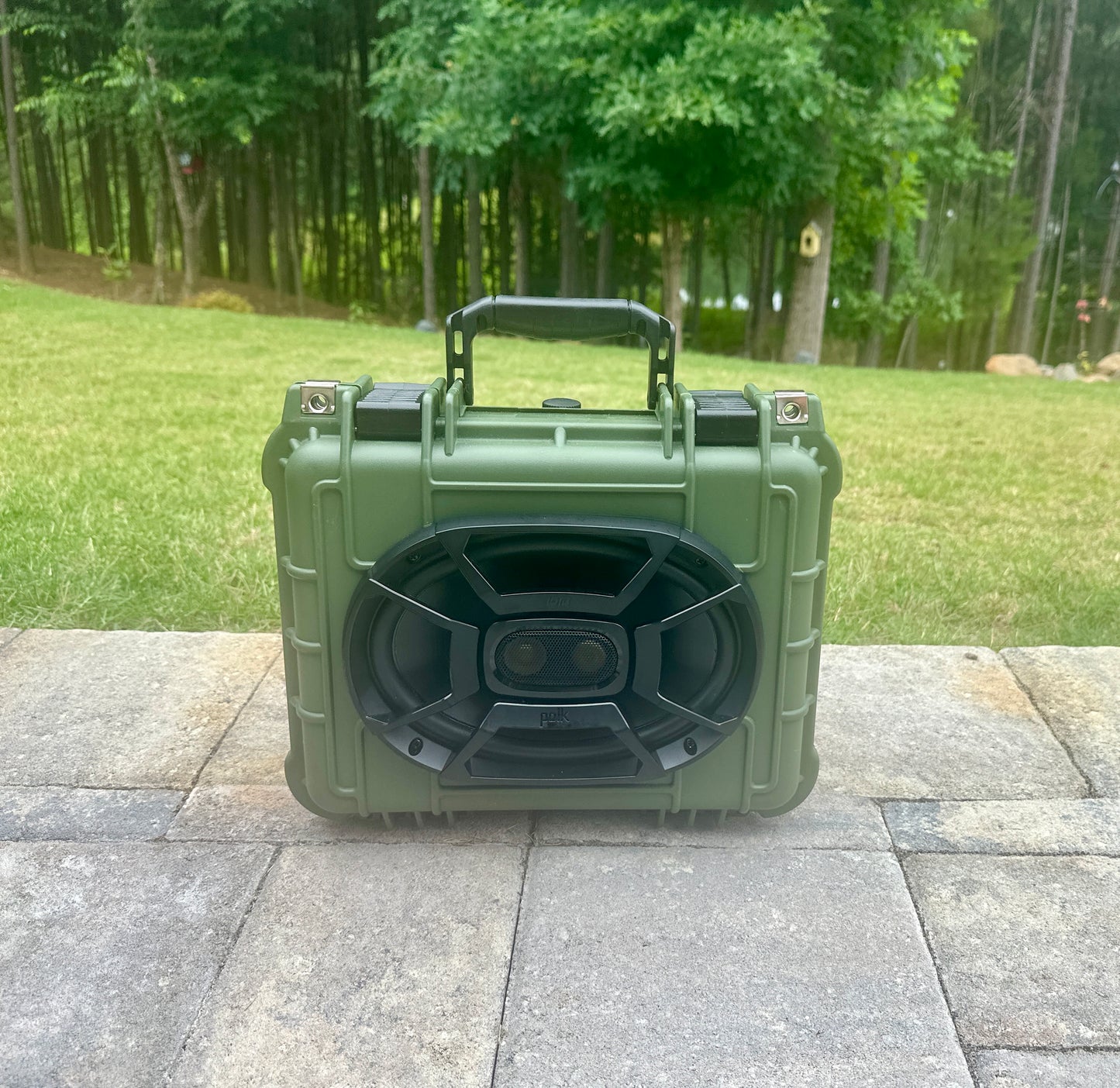 Green portable speaker on a stone surface with a grassy area and trees in the background